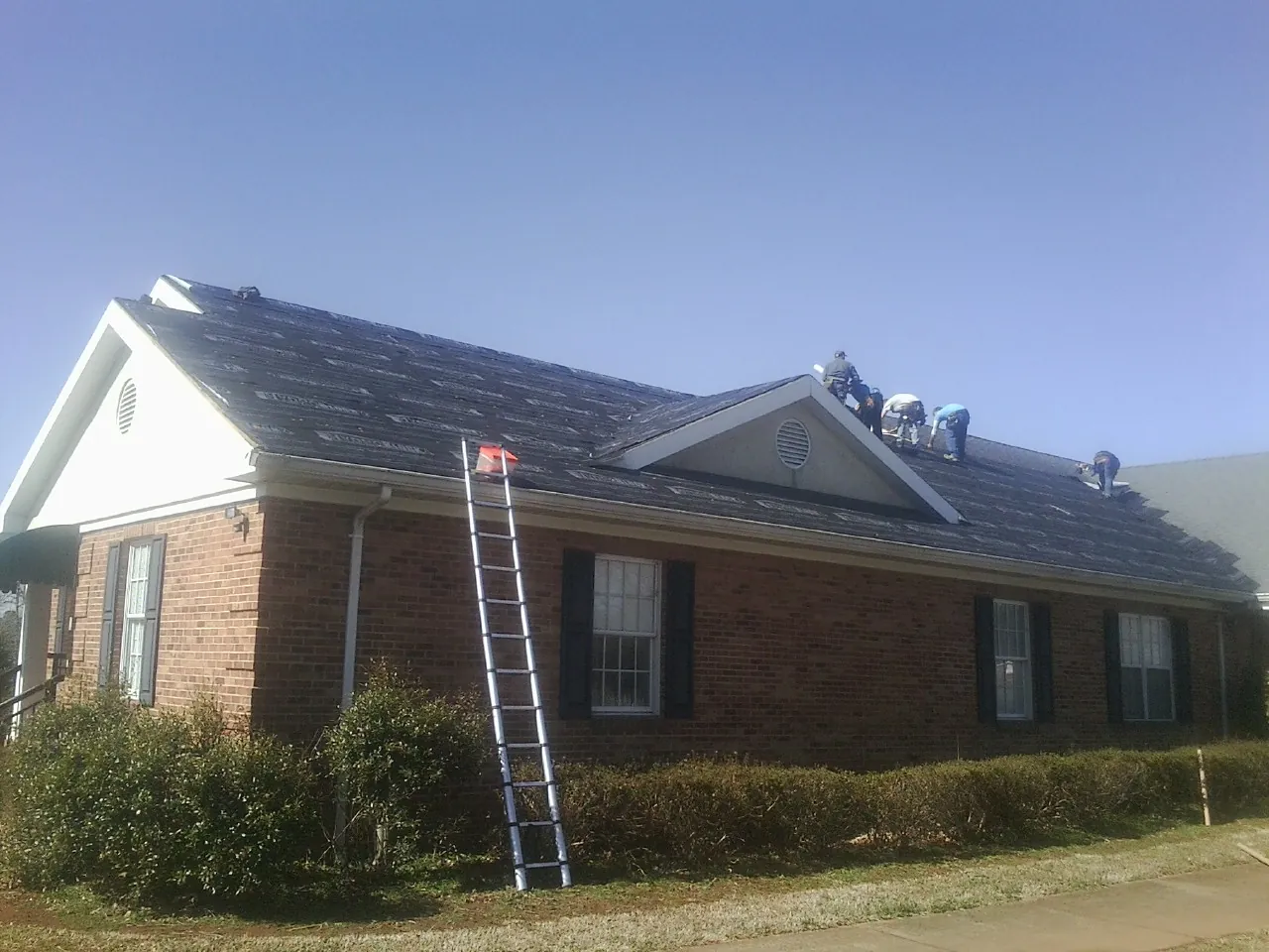 Crew tearing shingles off a brick ranch roof with a ladder set — Metal Roof Repair work by our crew in Dodge